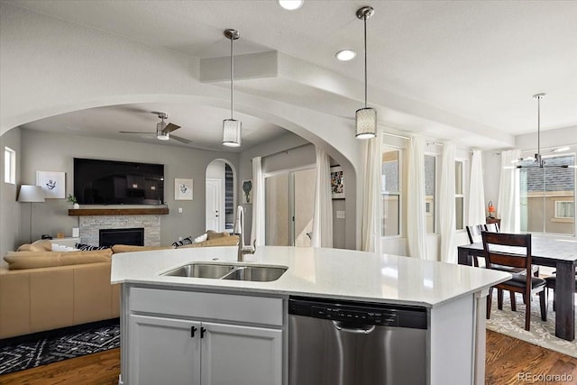 kitchen with arched walkways, a sink, open floor plan, dark wood-style flooring, and stainless steel dishwasher