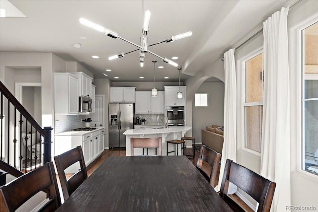 dining area featuring arched walkways, recessed lighting, dark wood-style flooring, stairs, and a notable chandelier
