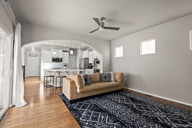 living area featuring arched walkways, a ceiling fan, recessed lighting, light wood finished floors, and baseboards