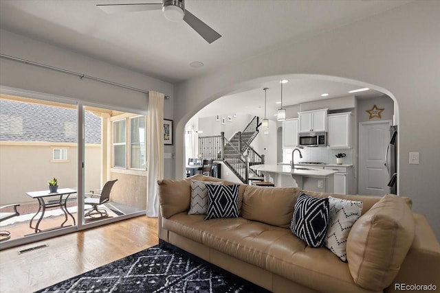 living area featuring a ceiling fan, stairs, visible vents, arched walkways, and wood finished floors