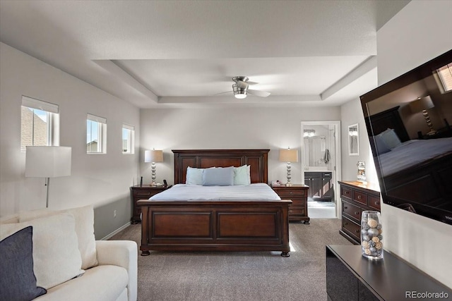 bedroom featuring carpet, connected bathroom, a tray ceiling, a ceiling fan, and baseboards