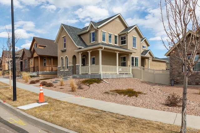 craftsman-style house with a porch, stucco siding, stone siding, and fence