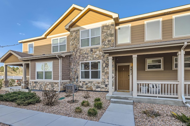craftsman house with a porch, central air condition unit, and stone siding