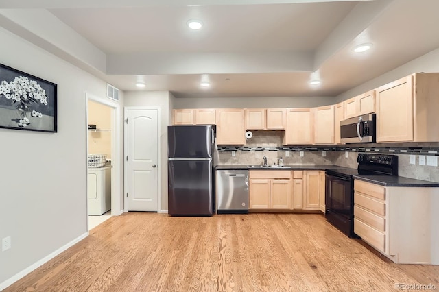kitchen with light wood-style floors, light brown cabinetry, dark countertops, washer / dryer, and stainless steel appliances