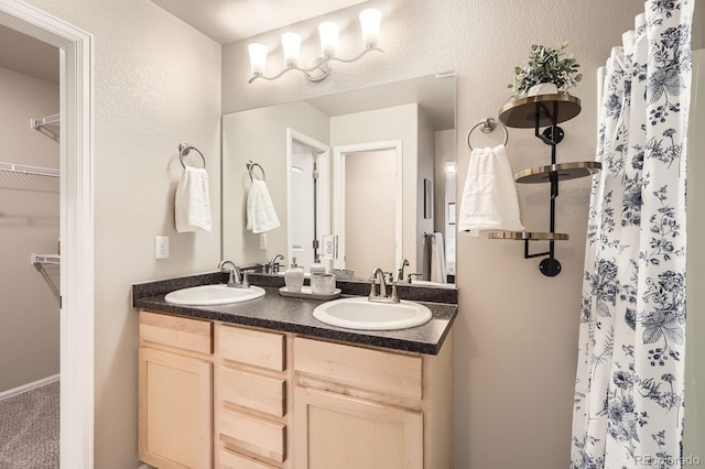 full bathroom with a spacious closet, double vanity, a sink, and curtained shower