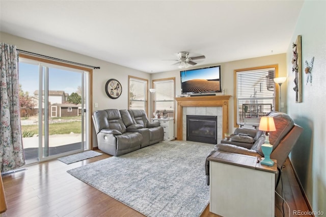 living area with ceiling fan, a tiled fireplace, and wood finished floors