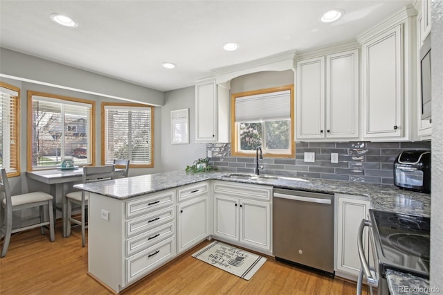 kitchen with a sink, dishwasher, range with electric cooktop, light wood-style flooring, and a peninsula