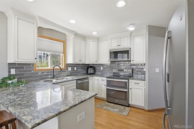 kitchen featuring a peninsula, white cabinetry, a sink, light wood finished floors, and stainless steel appliances