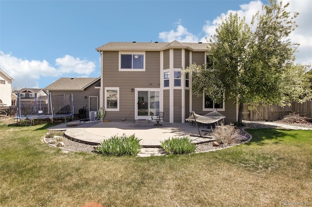 rear view of property with fence, a trampoline, a yard, and a patio