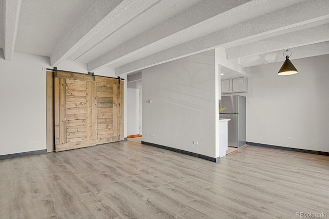 unfurnished living room with beam ceiling, light wood-style flooring, a textured ceiling, and baseboards