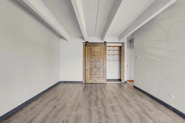 spare room featuring beam ceiling, a textured ceiling, wood finished floors, a barn door, and baseboards