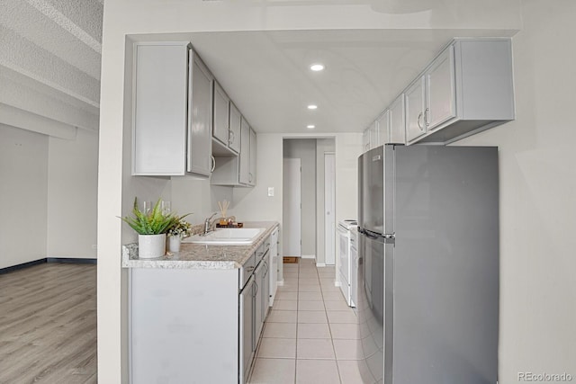 kitchen featuring baseboards, light countertops, recessed lighting, freestanding refrigerator, and a sink