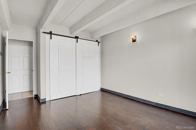 unfurnished bedroom with beamed ceiling, dark wood-type flooring, a textured ceiling, a barn door, and baseboards