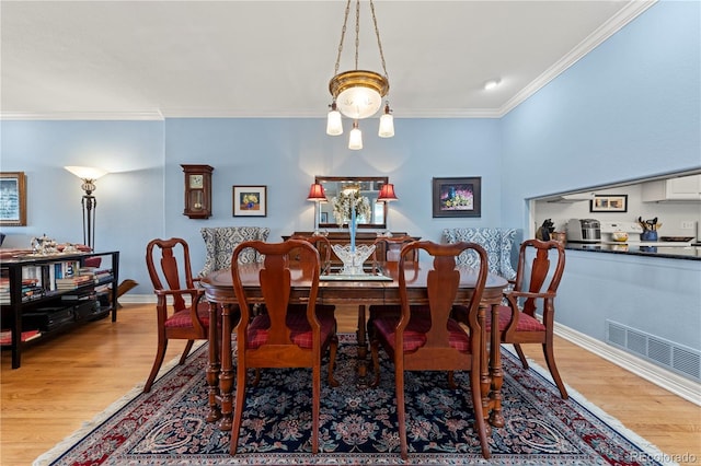 dining space with visible vents, light wood-style flooring, baseboards, and ornamental molding