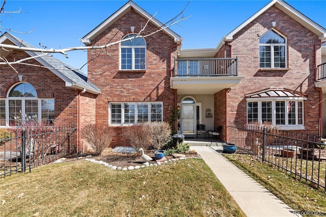 view of front of property with a front lawn, a balcony, fence, and brick siding