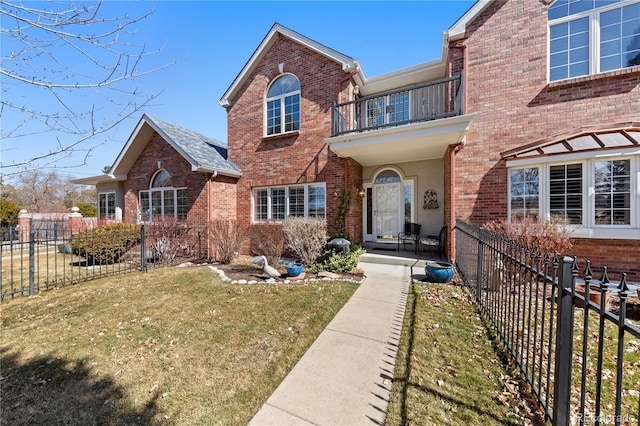 view of front of property featuring a front yard, brick siding, a balcony, and fence