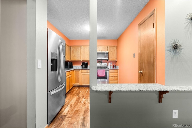 kitchen featuring a breakfast bar area, light hardwood / wood-style flooring, a textured ceiling, and appliances with stainless steel finishes