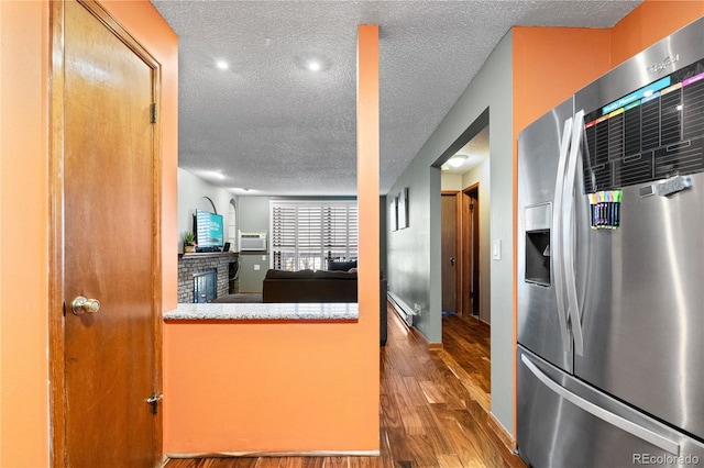 kitchen featuring an AC wall unit, stainless steel fridge, a textured ceiling, a baseboard radiator, and wood-type flooring