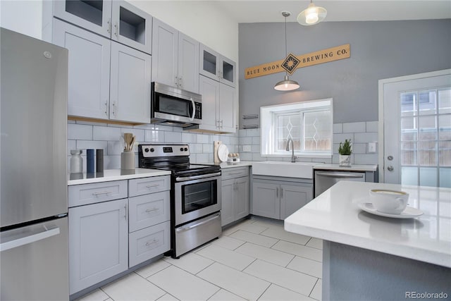 kitchen with gray cabinets, appliances with stainless steel finishes, pendant lighting, lofted ceiling, and decorative backsplash