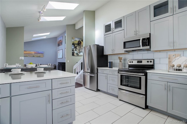 kitchen with gray cabinetry, tasteful backsplash, vaulted ceiling, light tile patterned floors, and stainless steel appliances