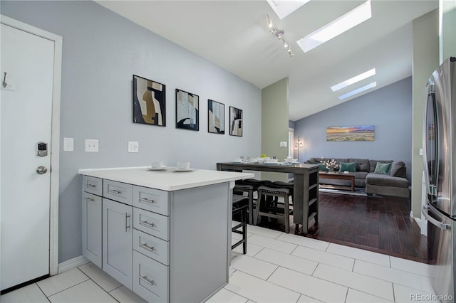 kitchen featuring gray cabinets, stainless steel refrigerator, a kitchen breakfast bar, vaulted ceiling with skylight, and kitchen peninsula