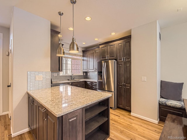 kitchen featuring light stone counters, light hardwood / wood-style floors, stainless steel fridge with ice dispenser, decorative light fixtures, and kitchen peninsula