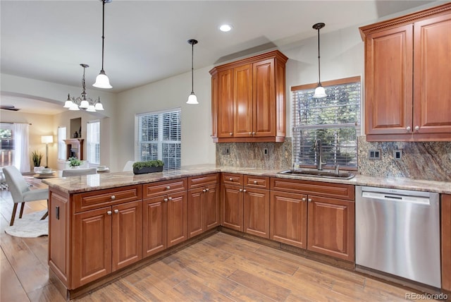 kitchen featuring brown cabinets, a peninsula, stainless steel dishwasher, light wood-style floors, and a sink