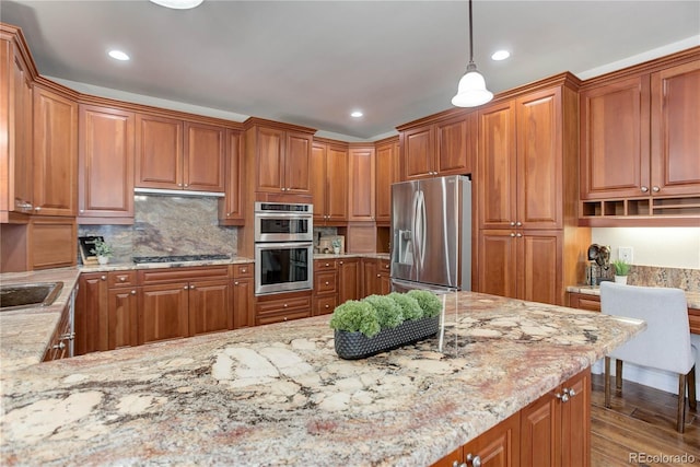 kitchen featuring stainless steel appliances, light stone counters, brown cabinetry, and wood finished floors