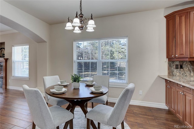 dining space with dark wood-style floors, arched walkways, a chandelier, and baseboards