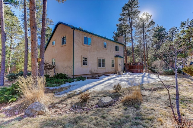 rear view of property with a deck, a chimney, and stucco siding