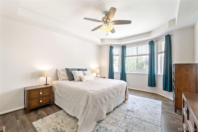 bedroom featuring dark wood-type flooring, a tray ceiling, and ceiling fan