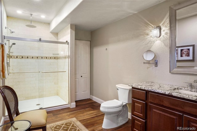 bathroom with a shower stall, wood finished floors, toilet, vanity, and baseboards