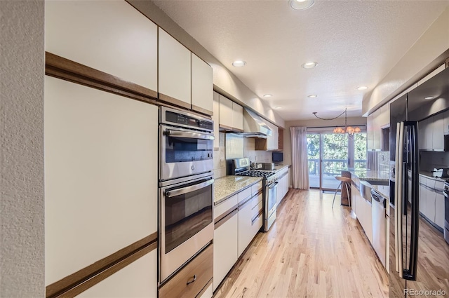 kitchen featuring hanging light fixtures, stainless steel appliances, white cabinetry, and light hardwood / wood-style flooring