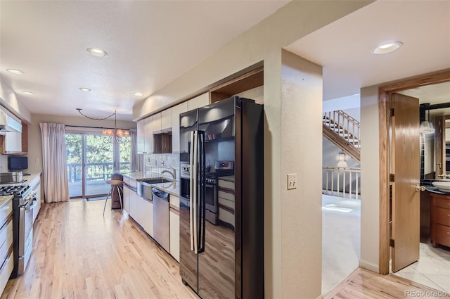 kitchen with tasteful backsplash, hanging light fixtures, stainless steel appliances, sink, and light wood-type flooring