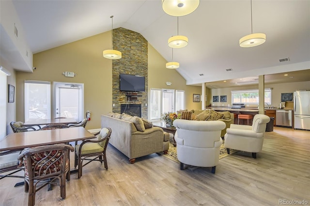 living room featuring sink, high vaulted ceiling, light hardwood / wood-style floors, and a stone fireplace