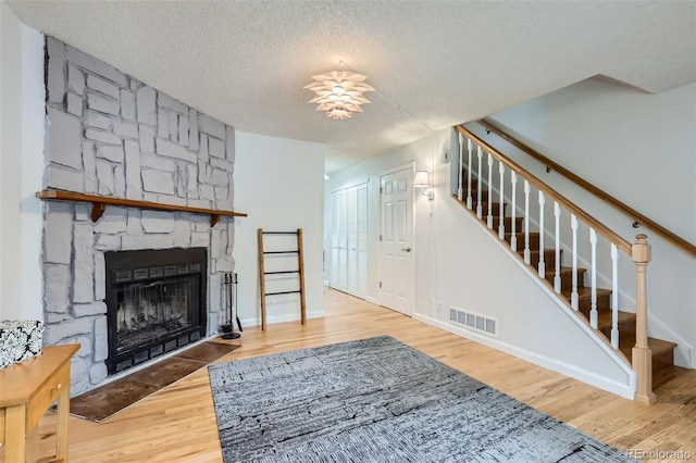 8136 Washington St Unit 141, Denver, CO 80229 - living area featuring wood finished floors, a stone fireplace, stairs, a textured ceiling, and baseboards