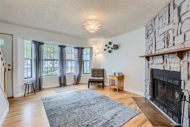 8136 Washington St Unit 141, Denver, CO 80229 - sitting room with a textured ceiling, light wood finished floors, a stone fireplace, and baseboards