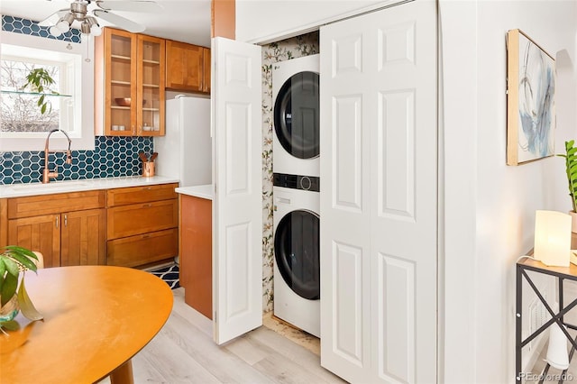 washroom with stacked washer and dryer, light hardwood / wood-style floors, sink, and ceiling fan