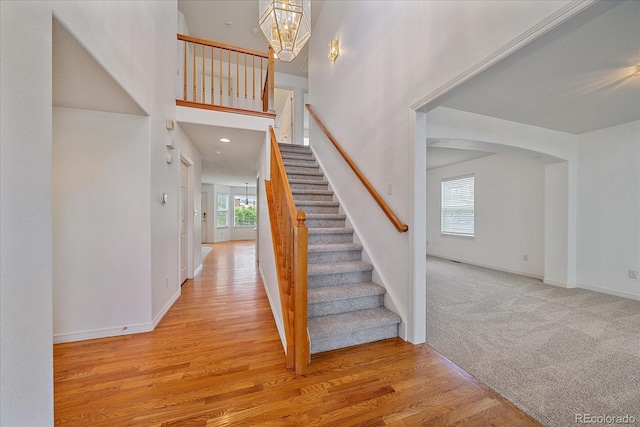 stairs featuring a chandelier, baseboards, a healthy amount of sunlight, and wood finished floors