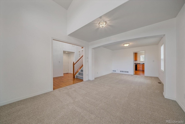 unfurnished room with light colored carpet, stairs, baseboards, and visible vents
