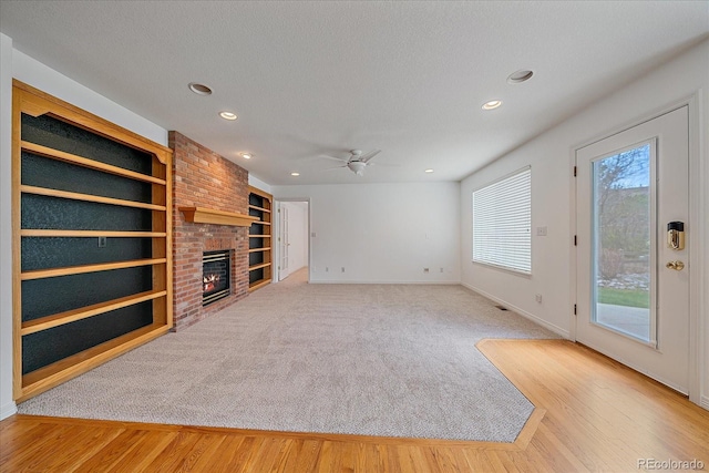 unfurnished living room with ceiling fan, recessed lighting, a brick fireplace, and wood finished floors