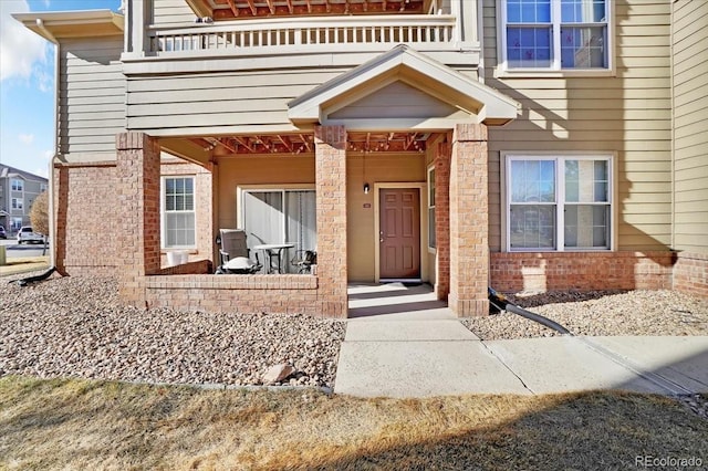 property entrance with brick siding, a porch, and a balcony