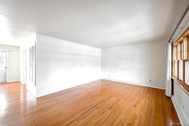 unfurnished room with baseboard heating and light hardwood / wood-style flooring