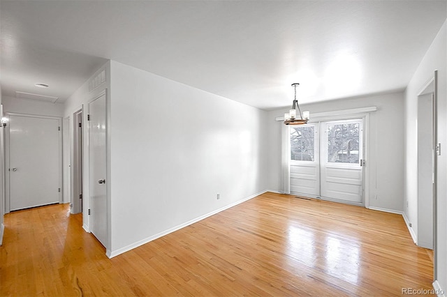 empty room featuring a notable chandelier and light wood-type flooring