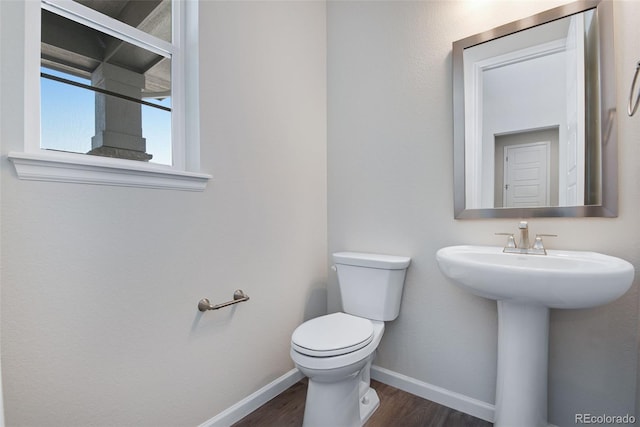 half bath featuring toilet, wood finished floors, baseboards, and a sink