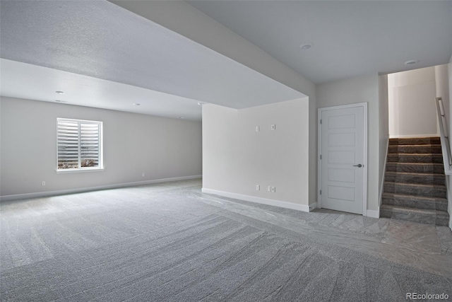 carpeted empty room featuring stairway and baseboards