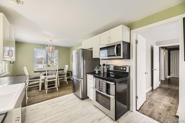 kitchen with white cabinets, stainless steel appliances, a sink, light wood-type flooring, and a notable chandelier