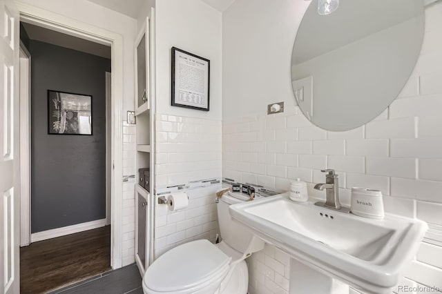 bathroom with tile walls, toilet, wood finished floors, and a sink