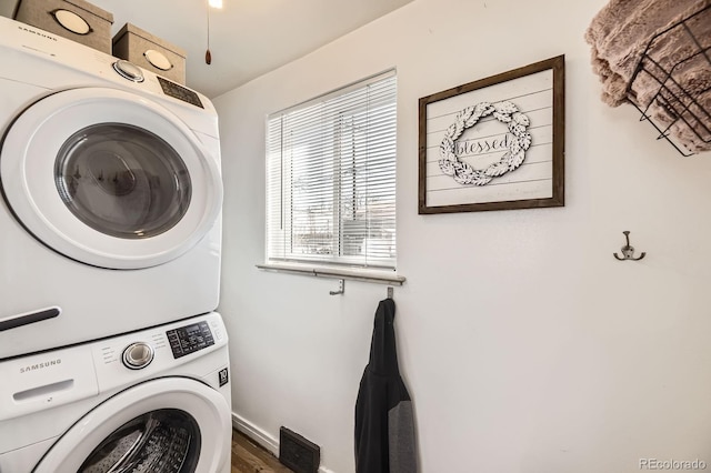 laundry room with baseboards, stacked washer / dryer, wood finished floors, and laundry area
