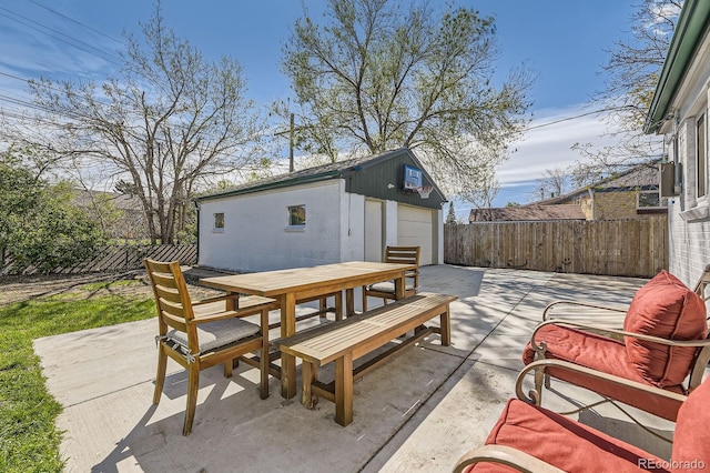 view of patio / terrace featuring fence private yard, a detached garage, an outbuilding, and outdoor dining space